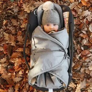 Blødt babyudstyr i grå farvetema med vinterhat, liggende på efterårsblade. Perfekt til kølige dage og udendørs eventyr for babyer.