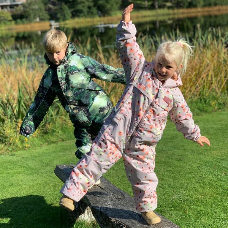 Legende børn i farverige jakker leger udendørs ved en sø i efteråret. Sjove øjeblikke med venskab og leg i naturen.