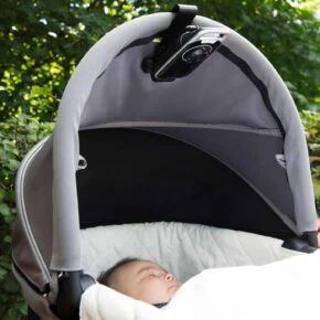 Rolig baby i barnevogn i naturen med solskærm.