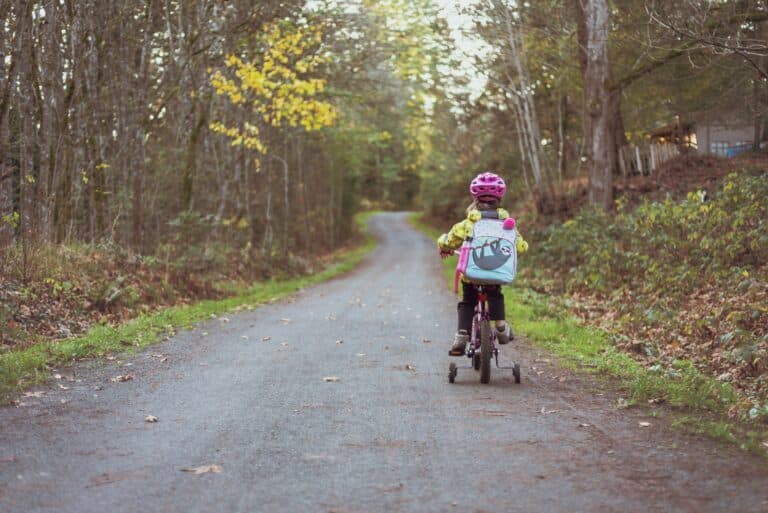 Glad pige på cykel i skovsti med bagage på ryggen.