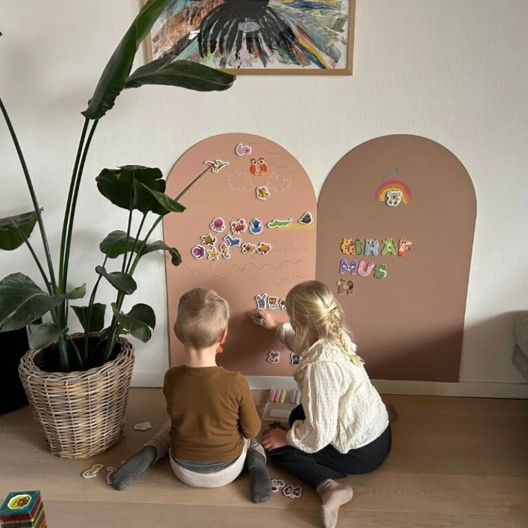 Farverige børn leger med magneter på en magnetvæg i hjemmet. Kreativ og lærerig aktivitet for små børn. Begynderbaby design, børnevenligt interiør.