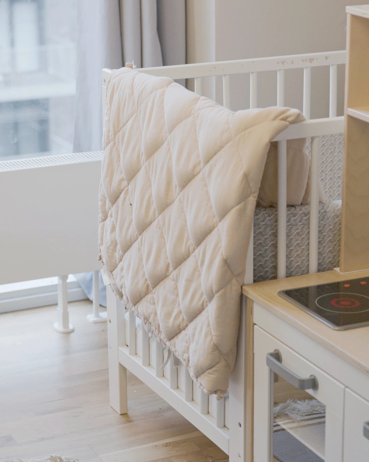 Blødt babytæppe hænger på tremmeseng i børneværelse.