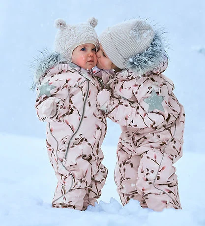 Billed af to små børn i vinterdress og huer i sneen, der leger udendørs.